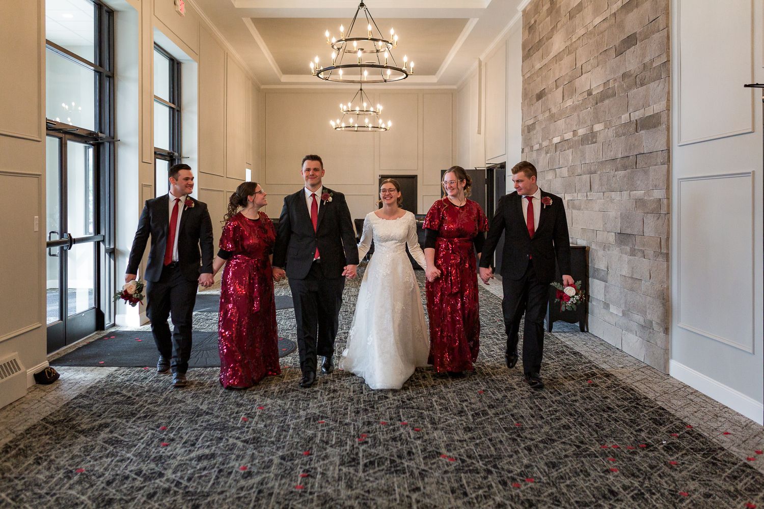 Elegant indoor wedding party photo with chandelier and stone accent wall.