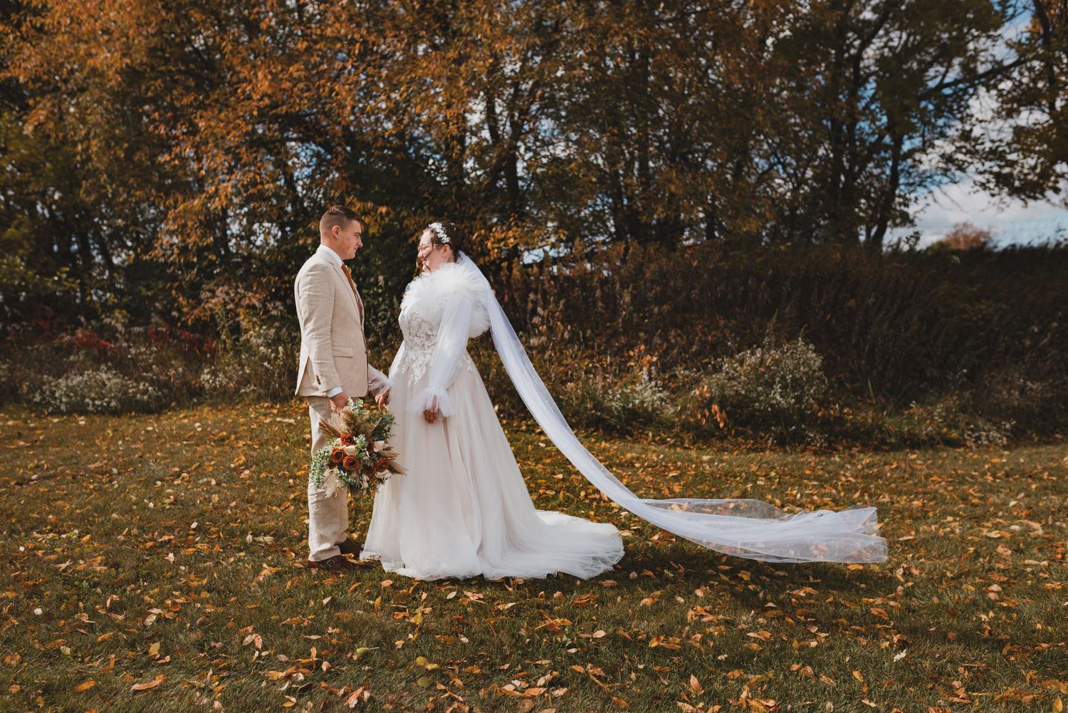 Wedding couple walking through autumn foliage during outdoor photo session.