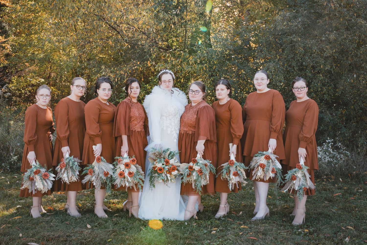 Wedding party poses outdoors in burgundy and white attire against autumn foliage.