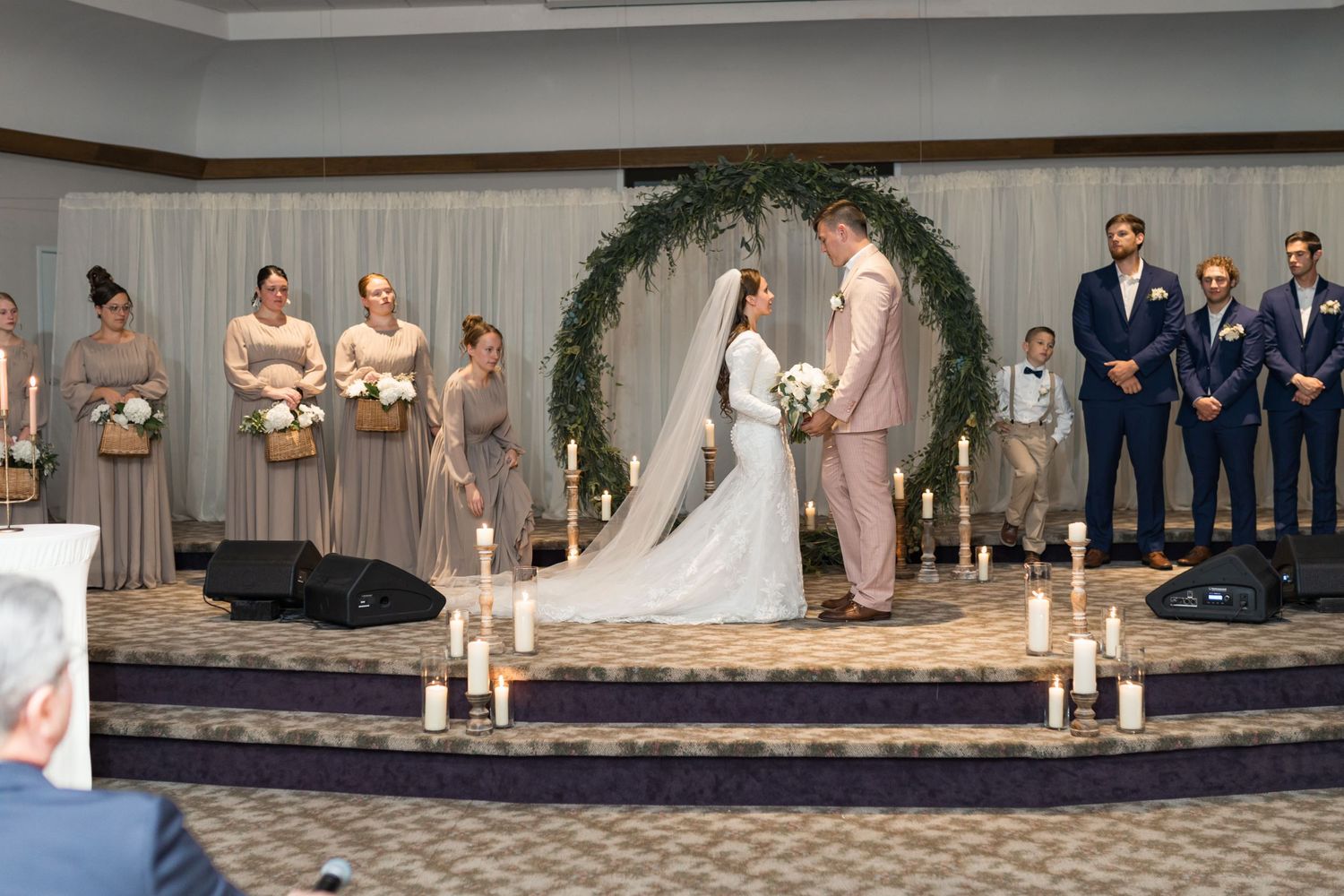 Wedding ceremony and reception in elegant indoor venue with stage and decorative lighting.
