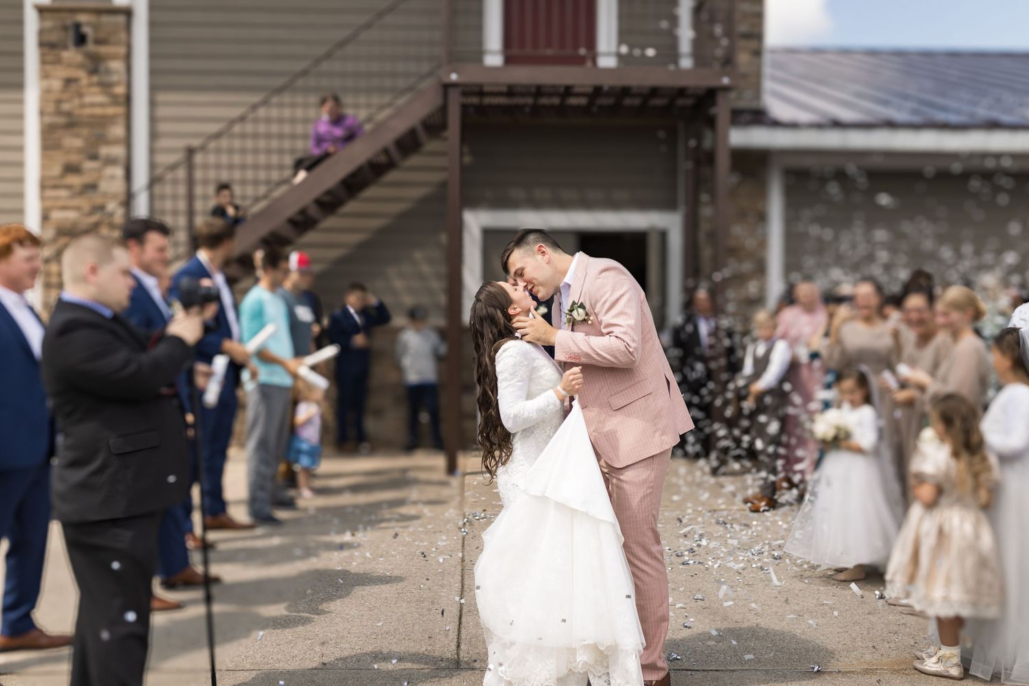 Wedding party group photo outside rustic venue during celebration.