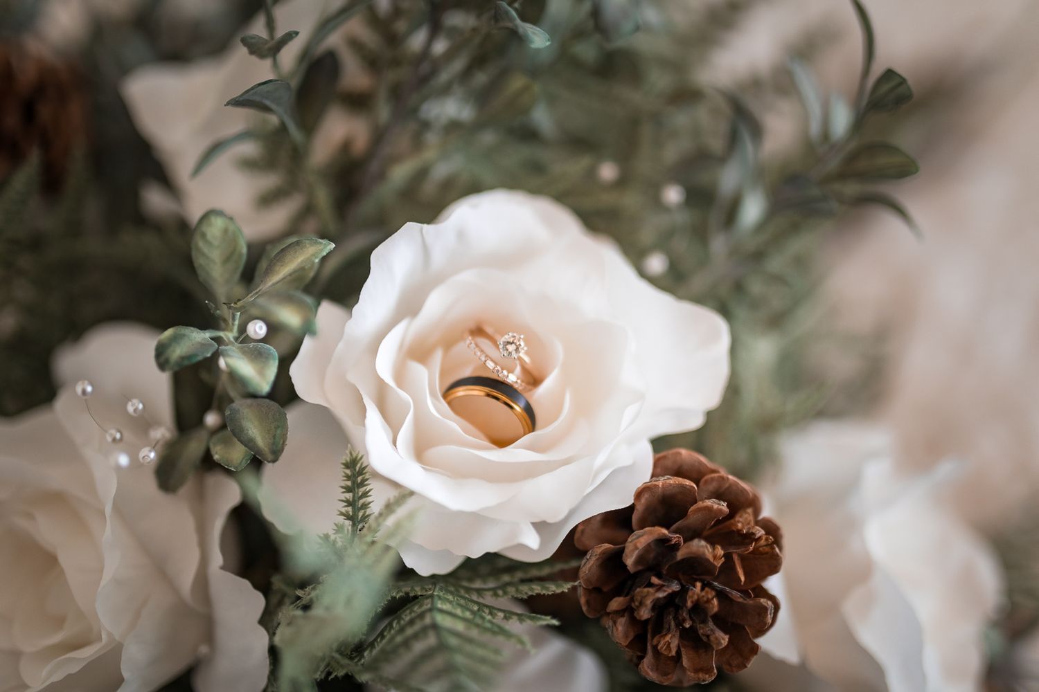 A white rose and pinecone arrangement with wedding rings nestled in the center of the bloom.