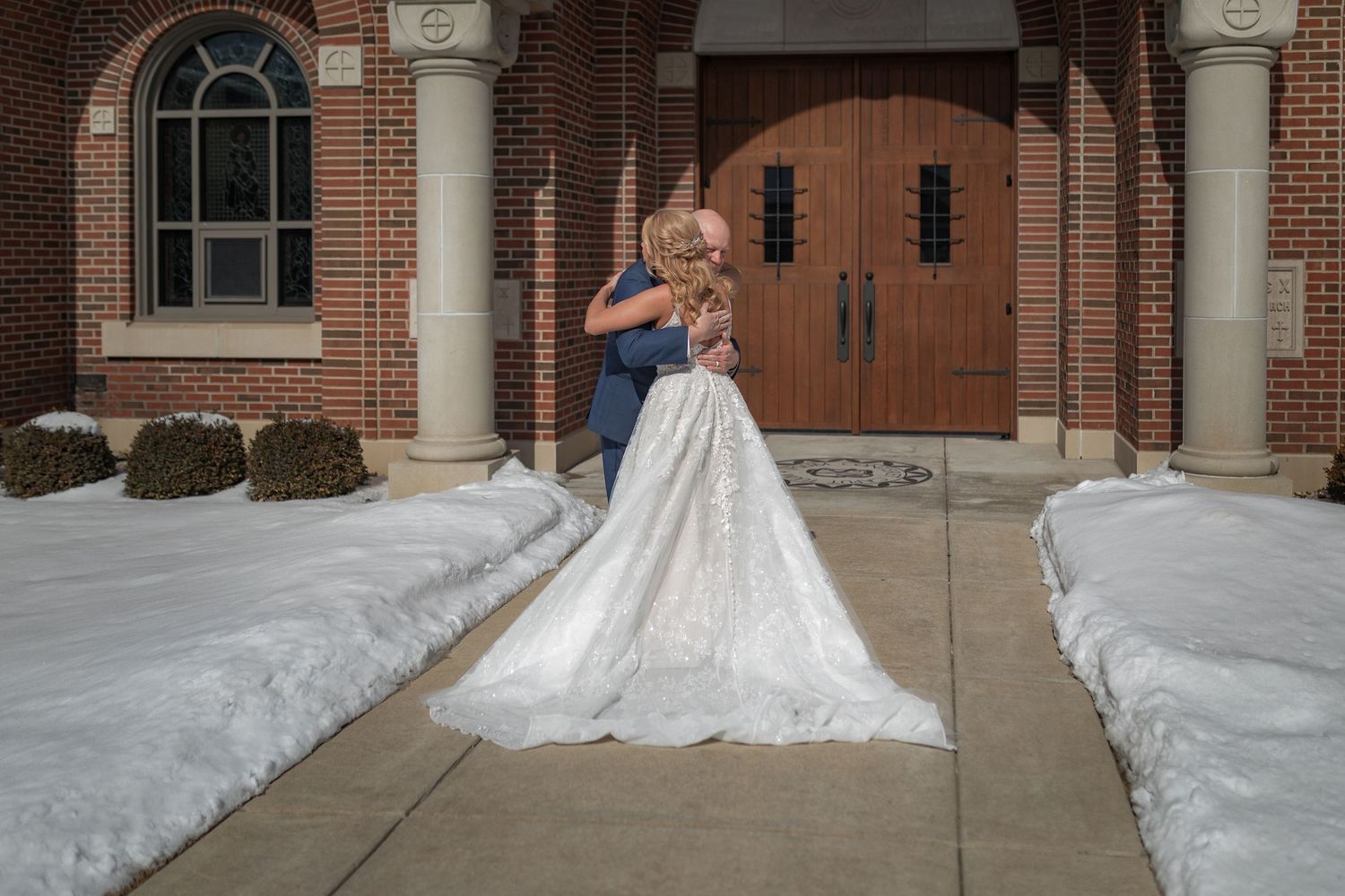 Long train of a white wedding dress trailing on concrete steps outside a brick building.