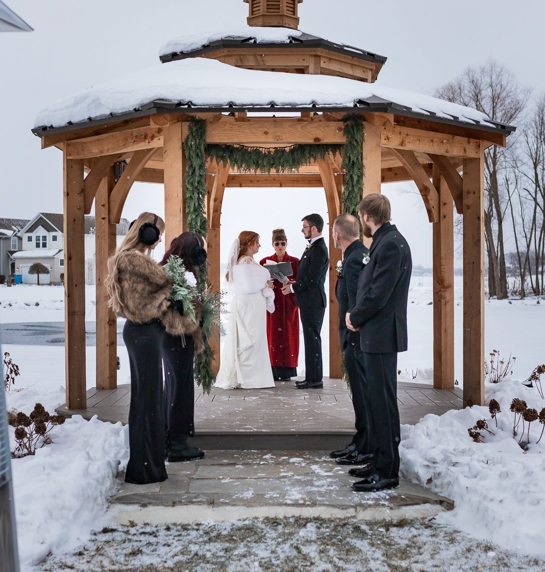 Snowy outdoor wedding ceremony at a rustic wooden pavilion overlooking a winter landscape.