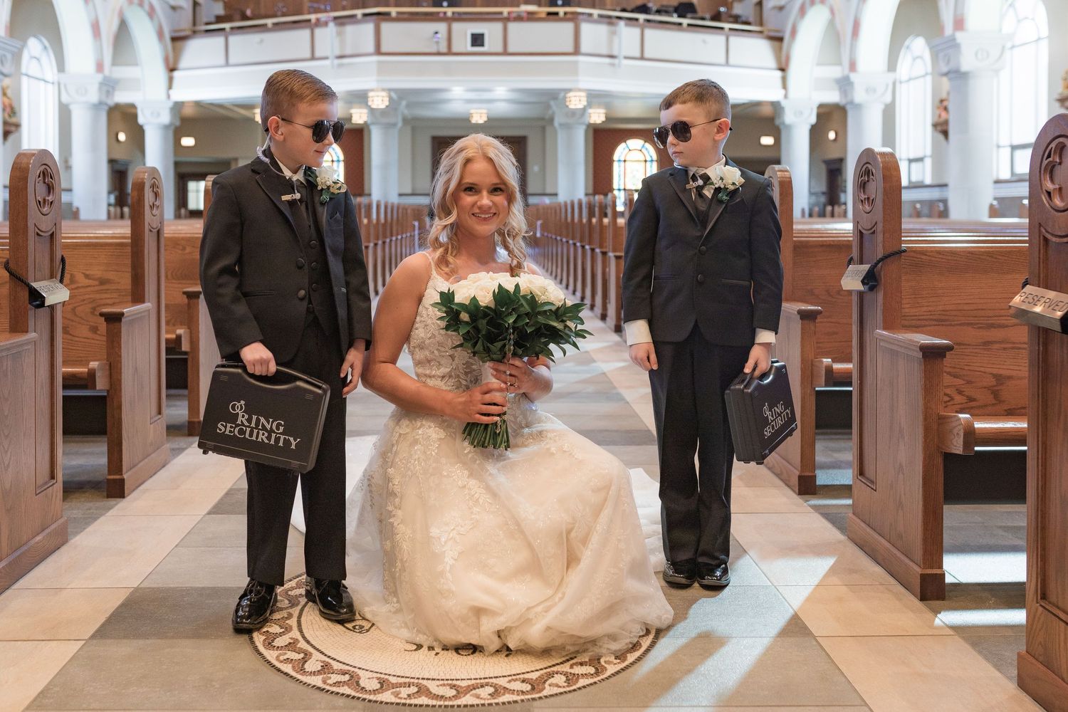 Wedding party gathered inside an elegant church with white columns and arched architecture.