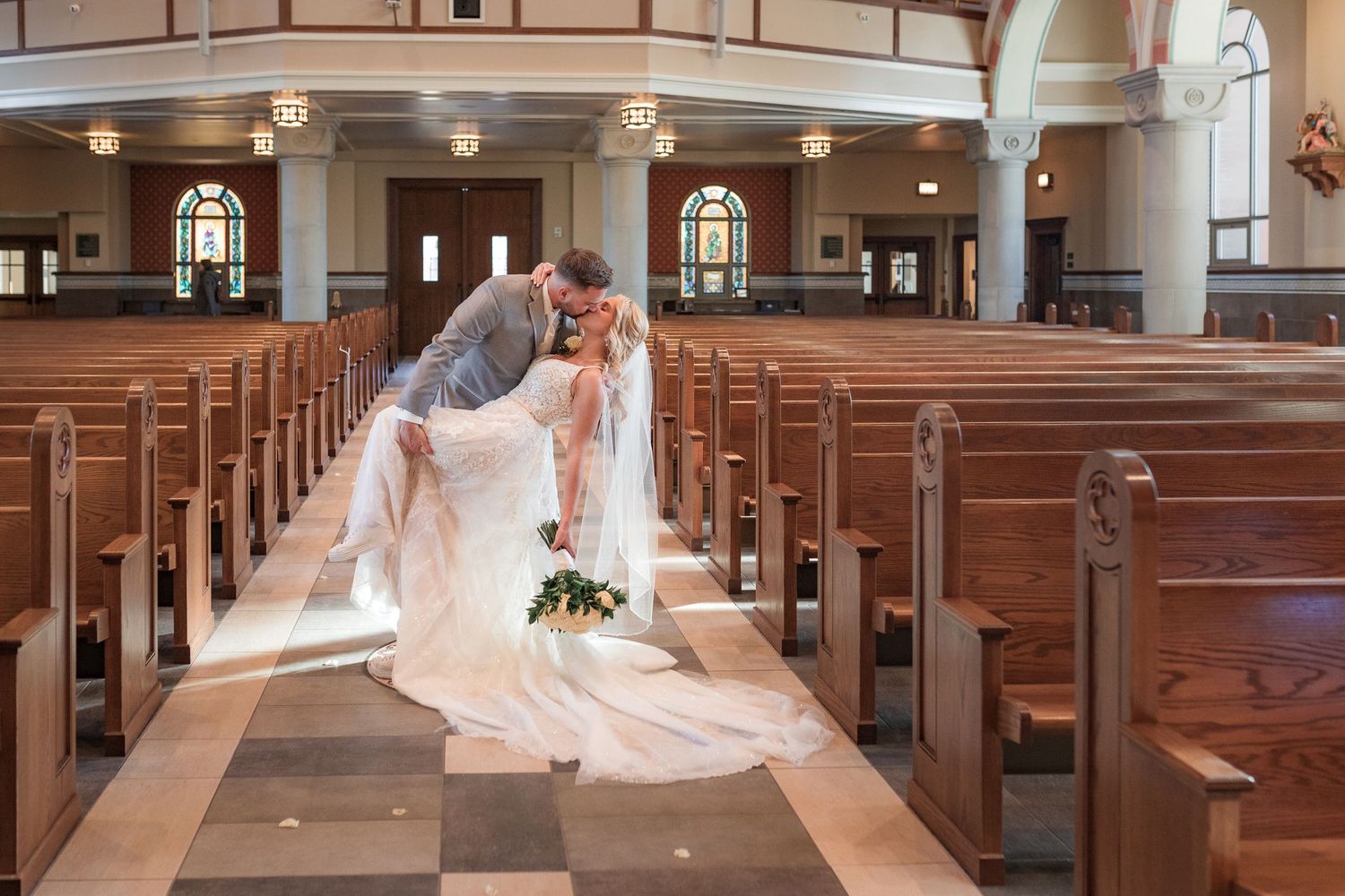 Long aisle of a church sanctuary with checkered flooring and wooden pews leading to an altar.