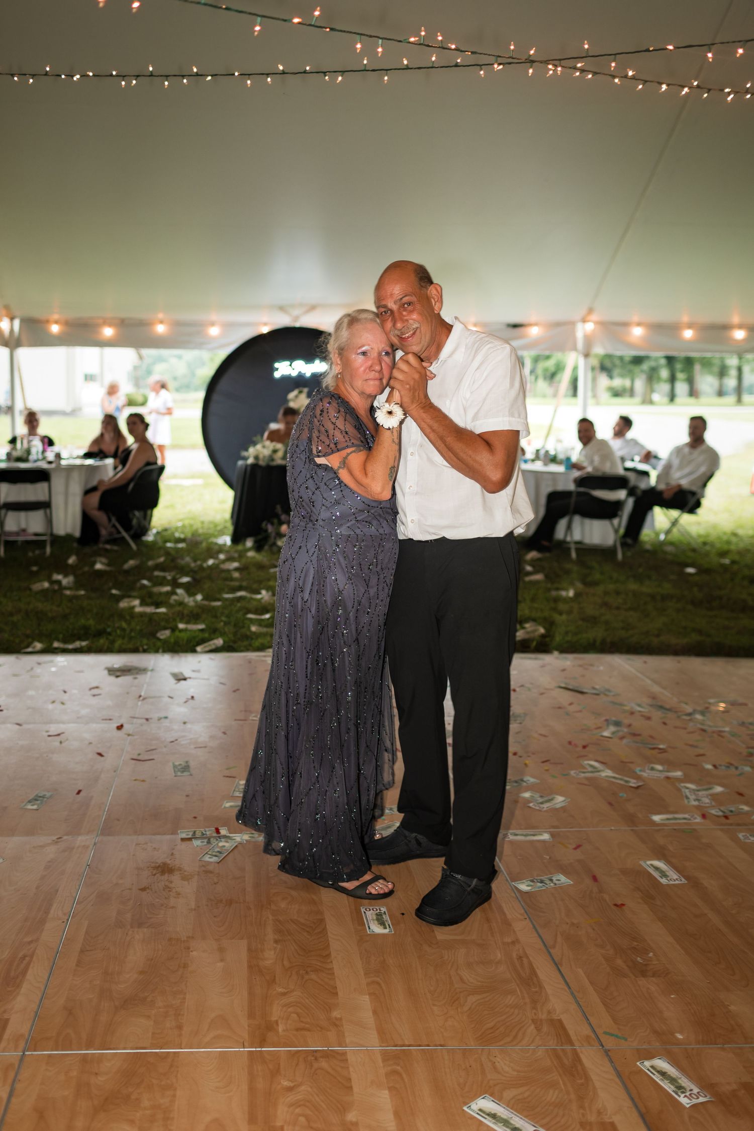 Couple slow dancing on a wooden dance floor under twinkling string lights at a wedding reception.