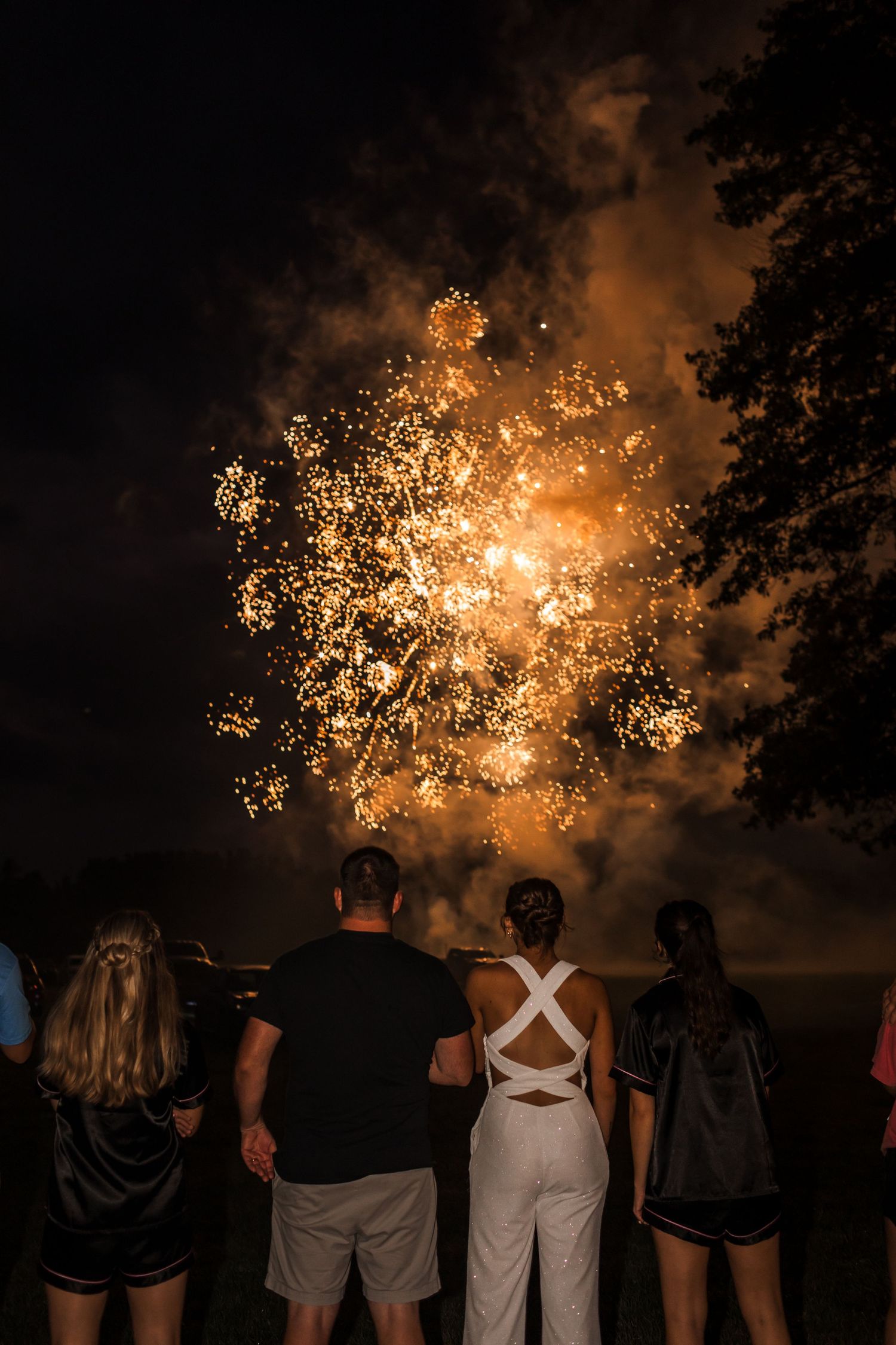 Silhouettes of wedding guests watching fireworks display against an orange night sky.