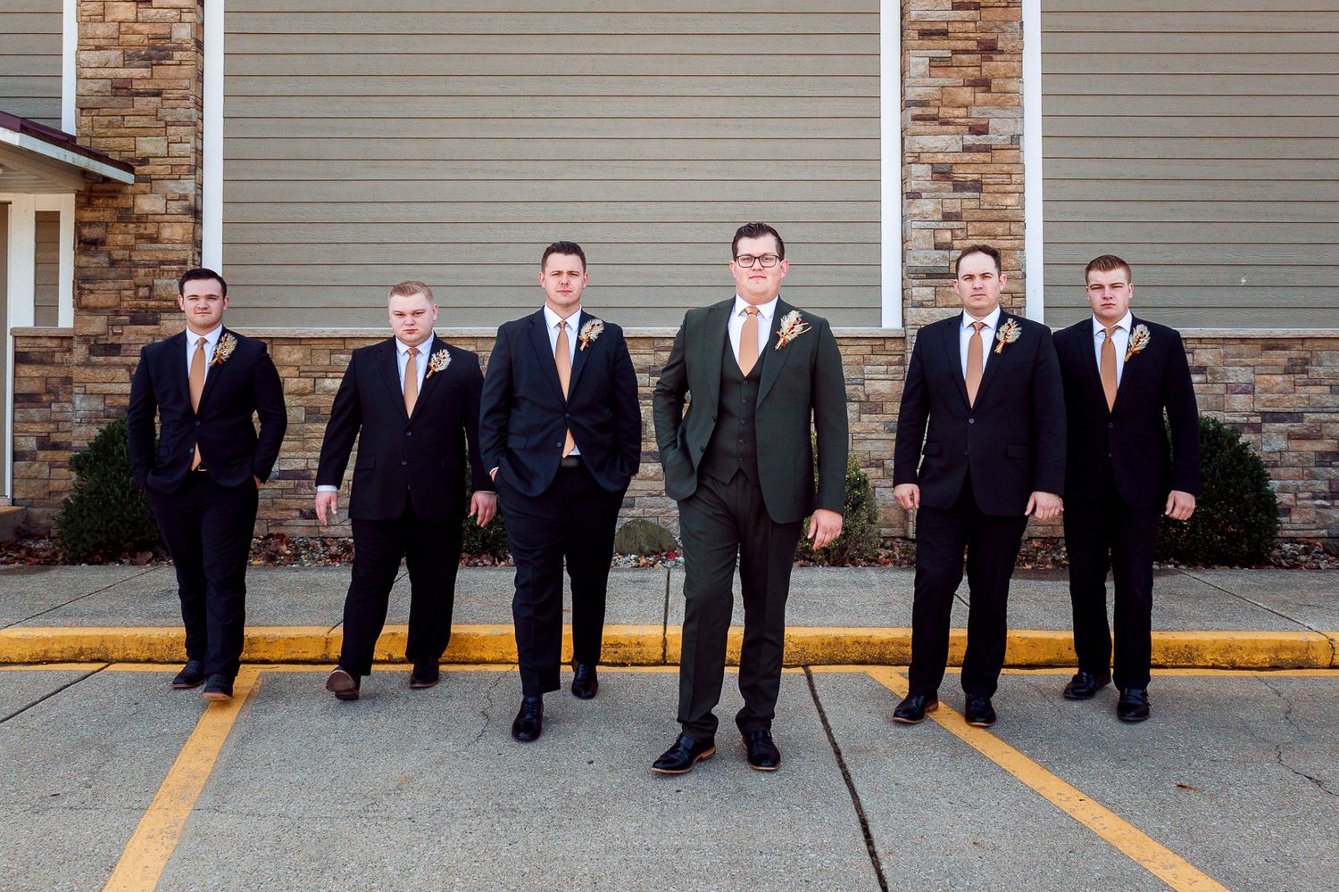 Groomsmen in dark suits posing in line on parking lot.
