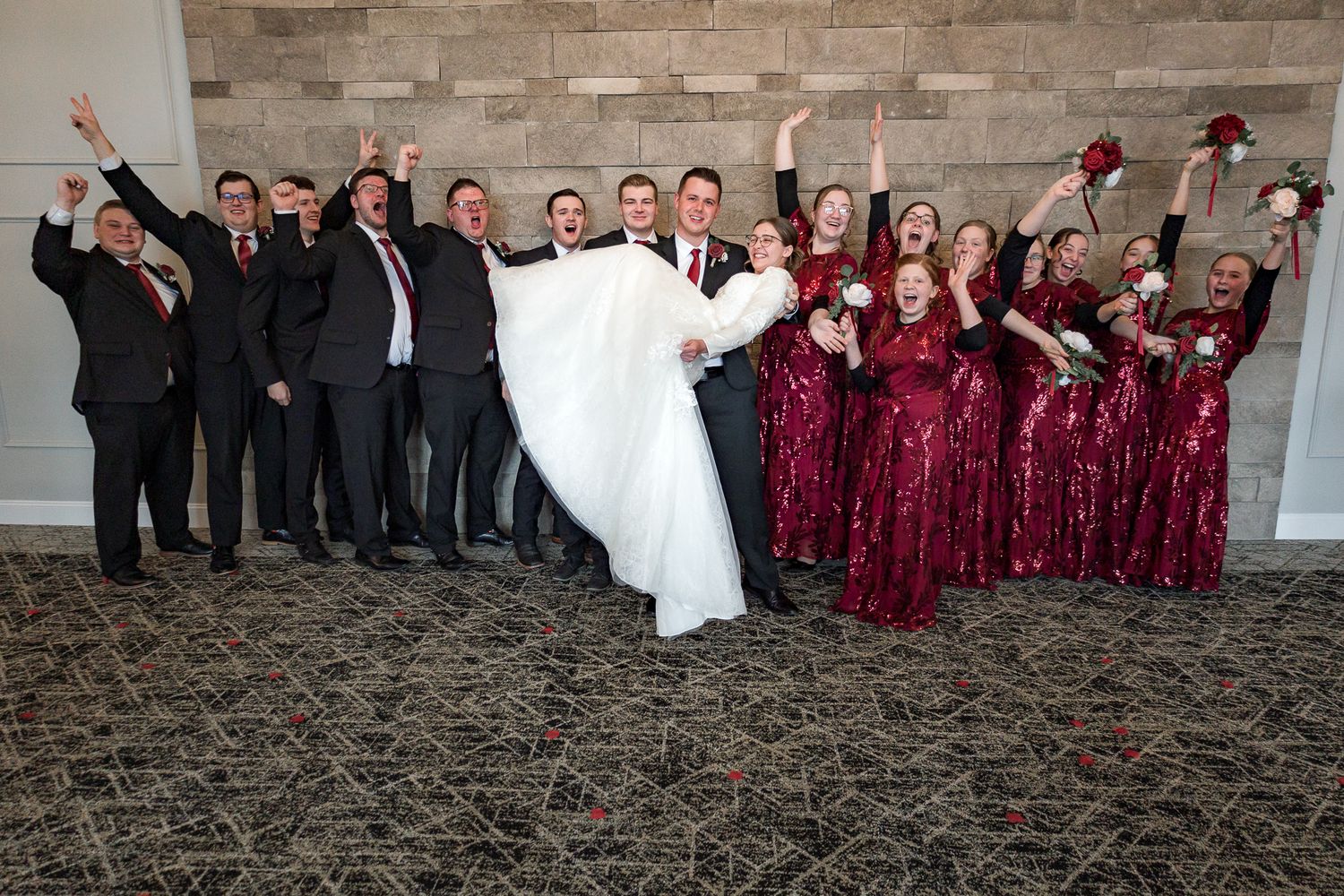 Wedding party in burgundy and black attire posing together for a group photo.