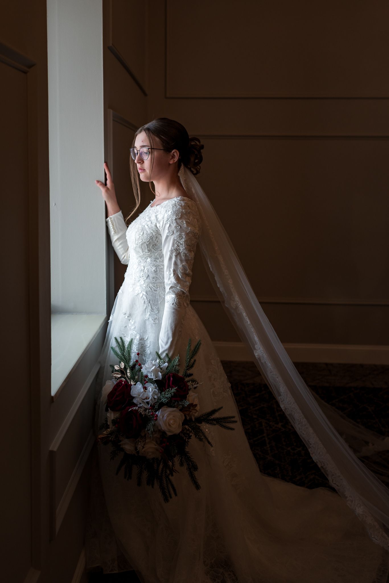 Silhouetted bride in a flowing white dress and veil standing by a window.