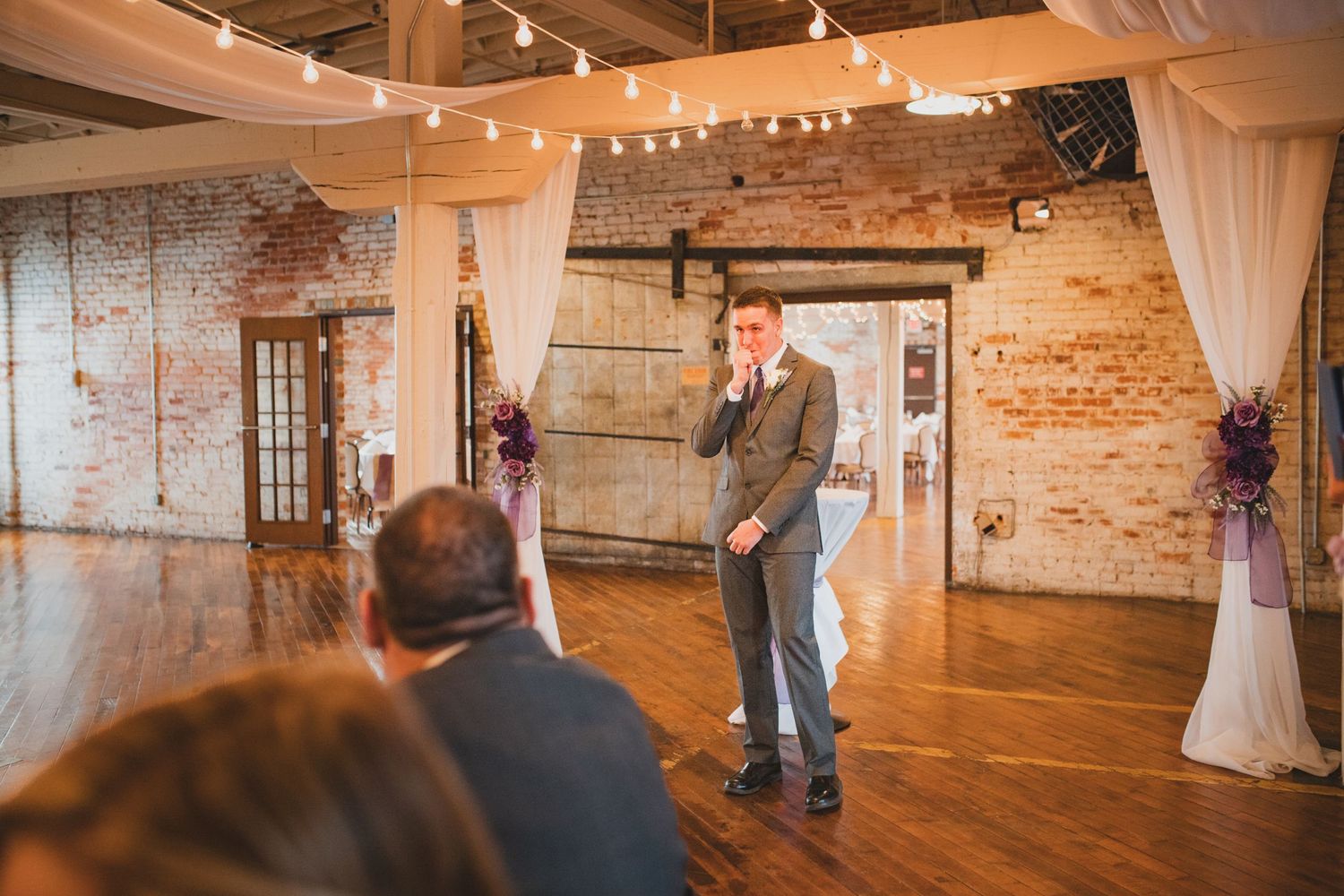 Wedding ceremony venue with exposed brick walls, hardwood floors and white fabric draping.