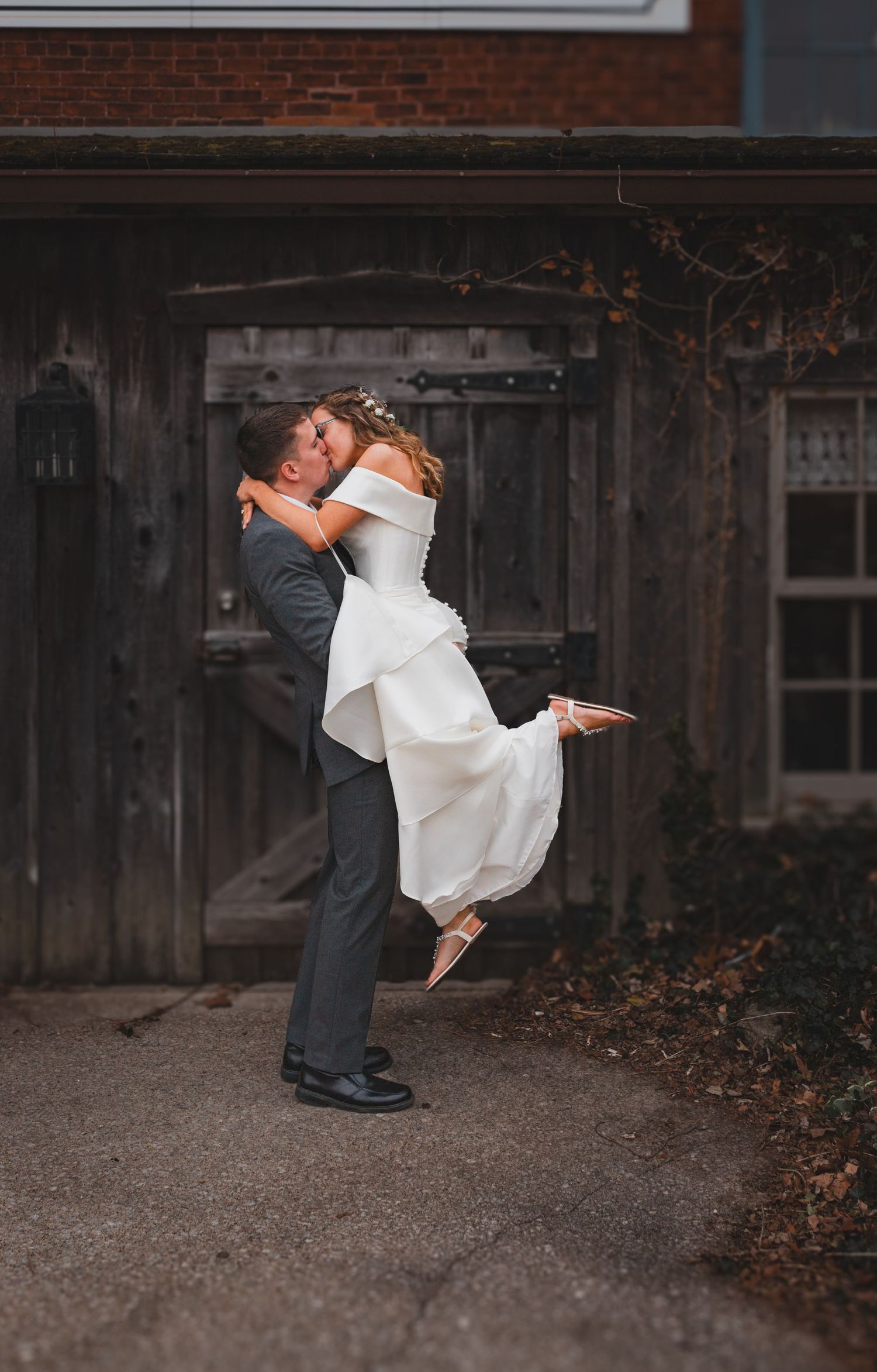 Romantic wedding photo of couple embracing in a playful spin pose against rustic backdrop.
