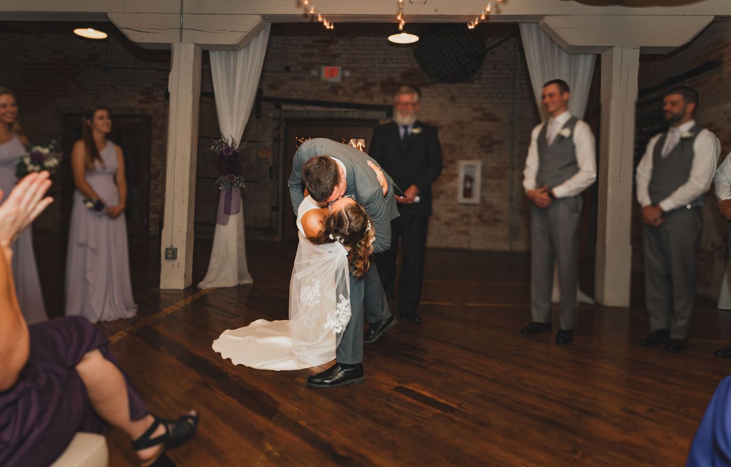 First dance moment at wedding reception in rustic venue with brick walls and string lights.