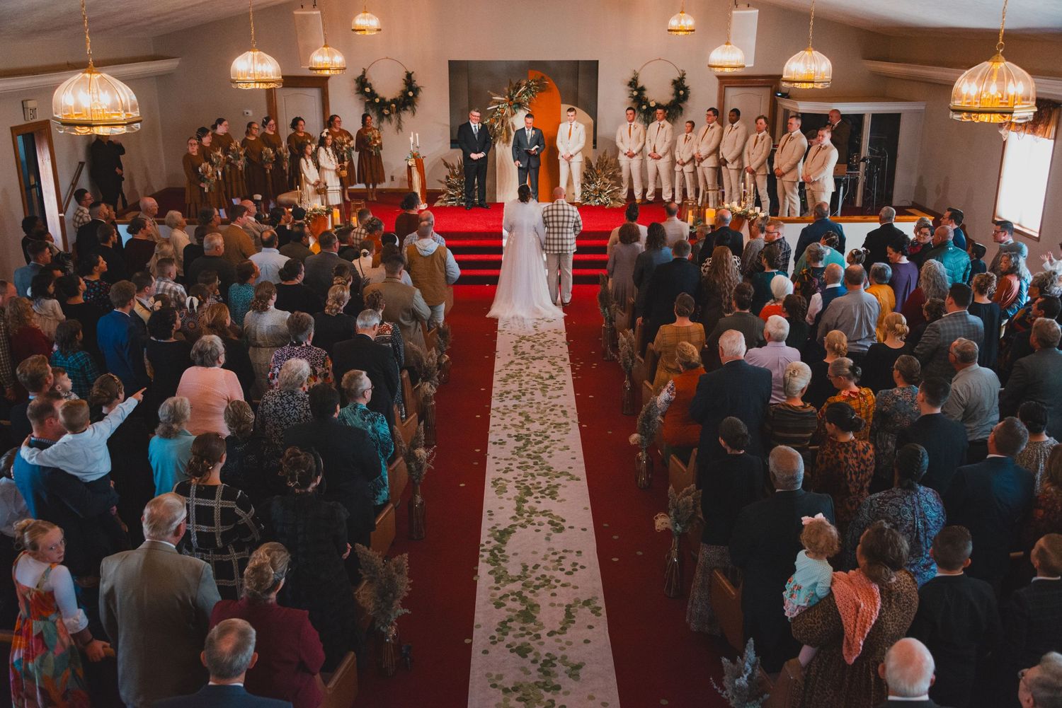 Overhead view of wedding ceremony with red carpet aisle and floral petals in packed venue.