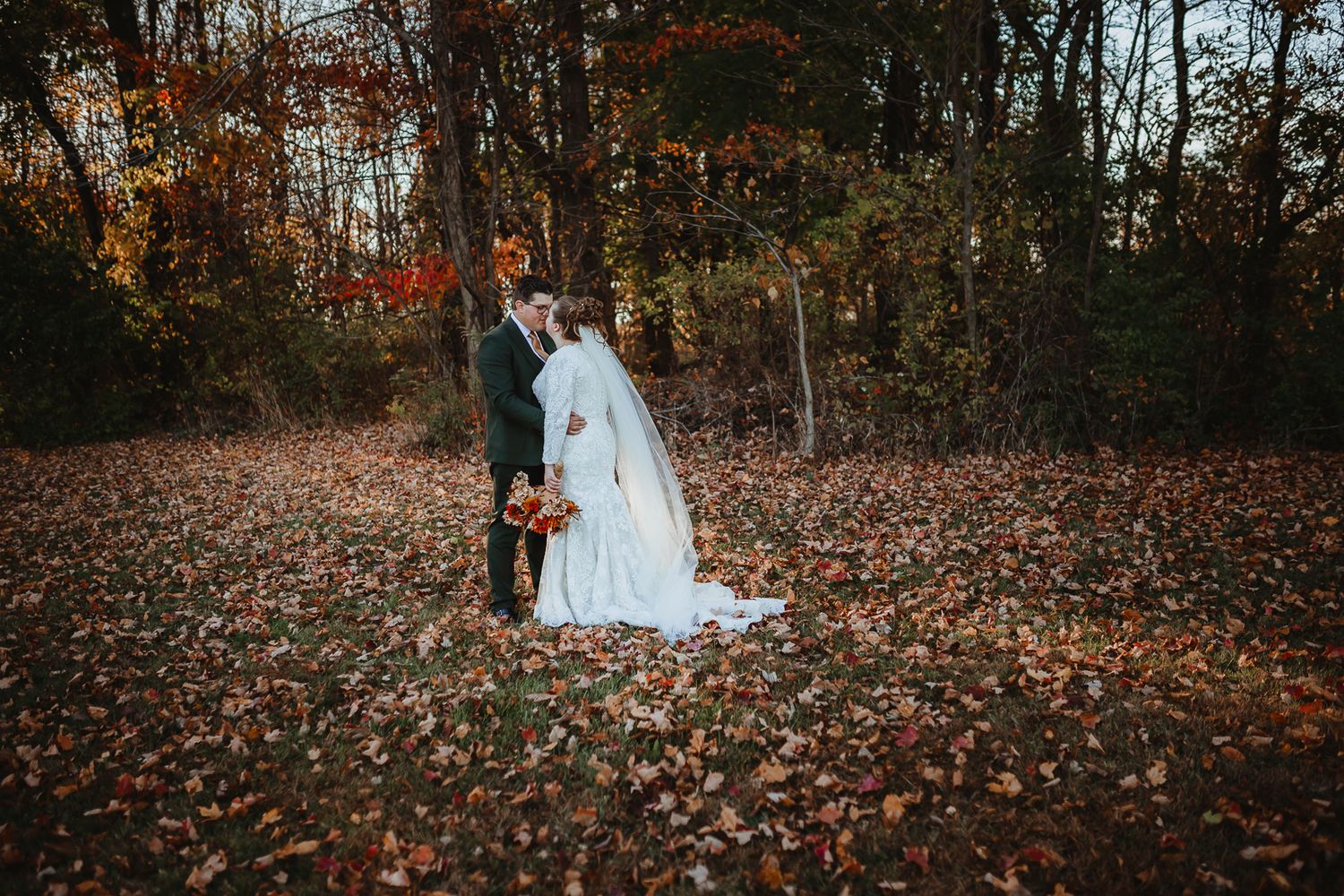 Wedding party poses together on ground covered in colorful autumn leaves.