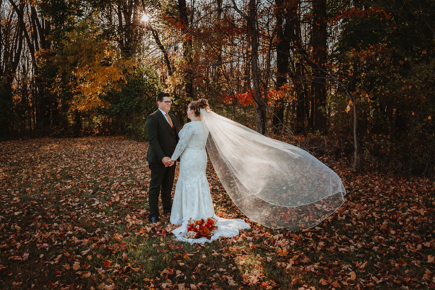 Autumn wedding portrait with flowing veil and fall foliage in wooded setting.