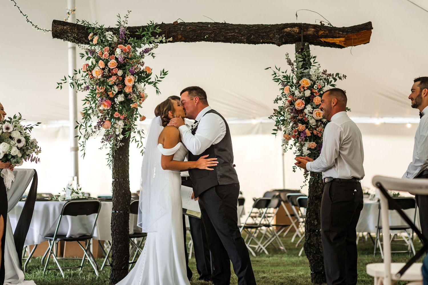 Wedding celebration under a tent with rustic wooden beams and floral decorations.