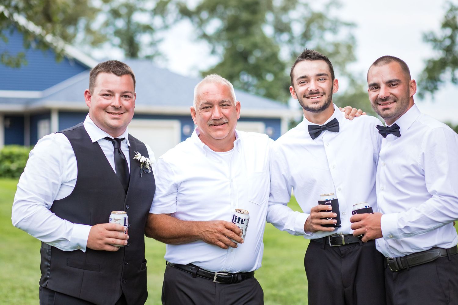 Groomsmen in formal attire holding drinks and celebrating outdoors at a wedding reception.