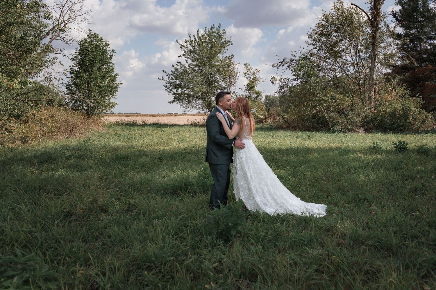 Summer wedding portraits in a green field with puffy clouds and natural landscape.