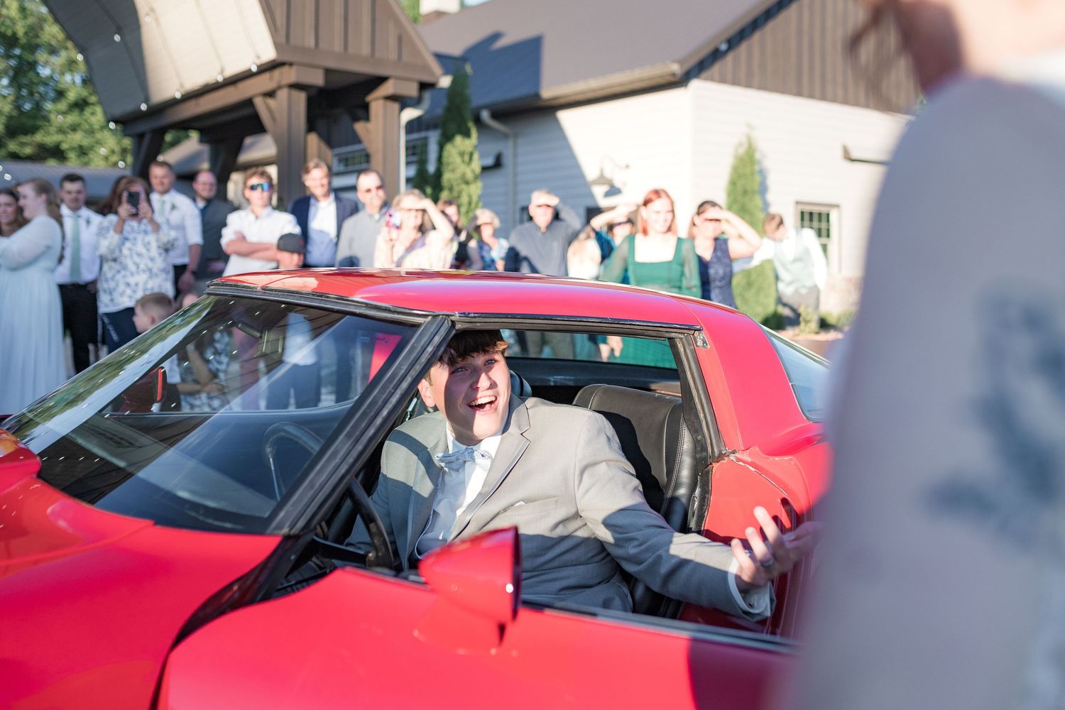 Wedding party departs in a bright red classic car as guests wave goodbye.