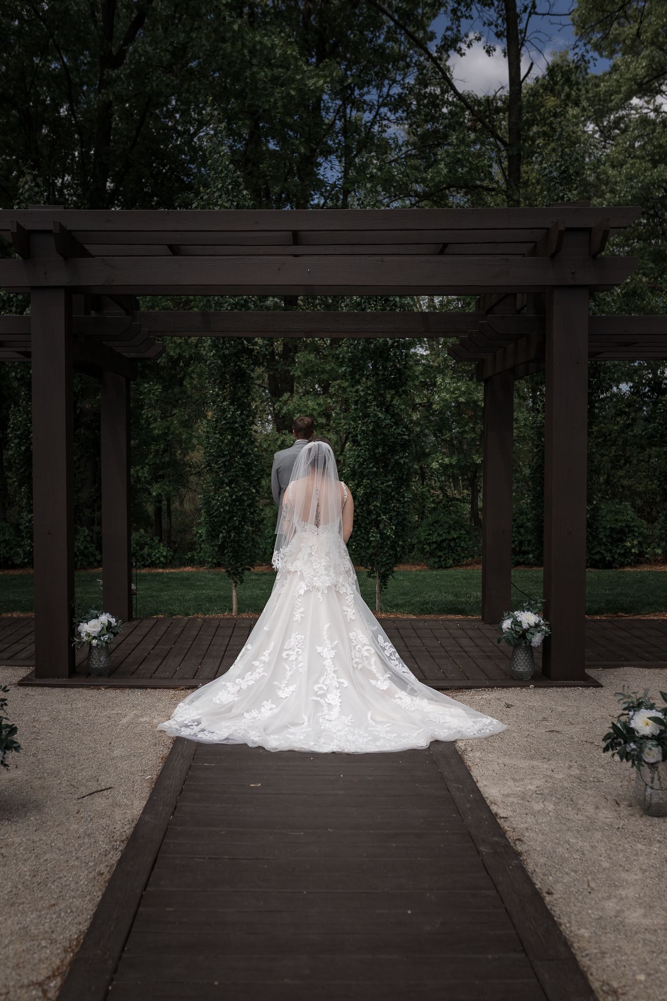 Long flowing wedding dress train photographed on wooden deck with garden backdrop.