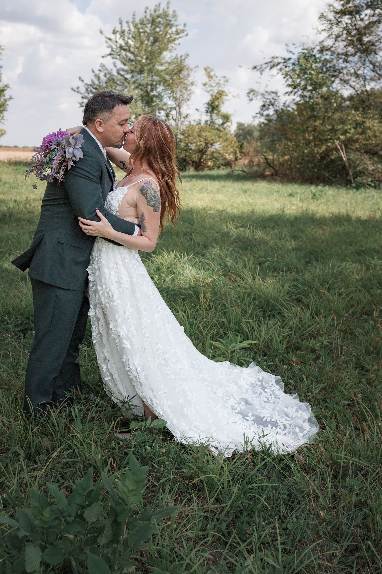 A romantic dip pose between newlyweds in a green meadow with the bride's dress flowing beautifully.