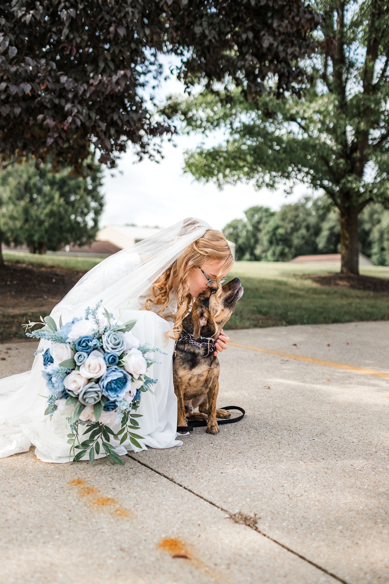 Wedding bouquet with blue and white flowers laid on concrete with a flowing white veil.