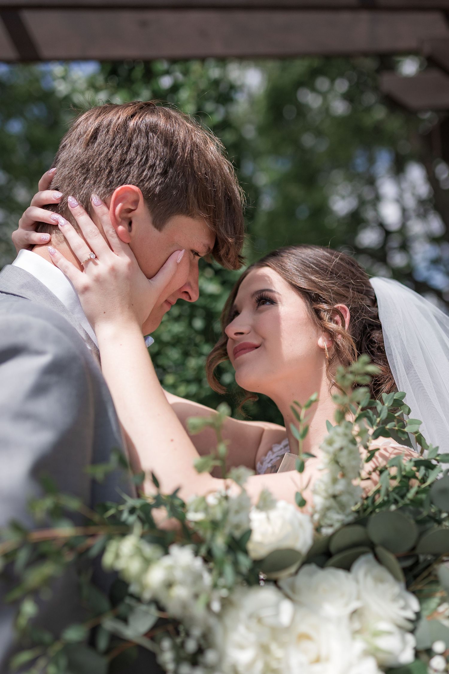 Romantic wedding couple shares intimate kisses among greenery and flowers in an outdoor setting.