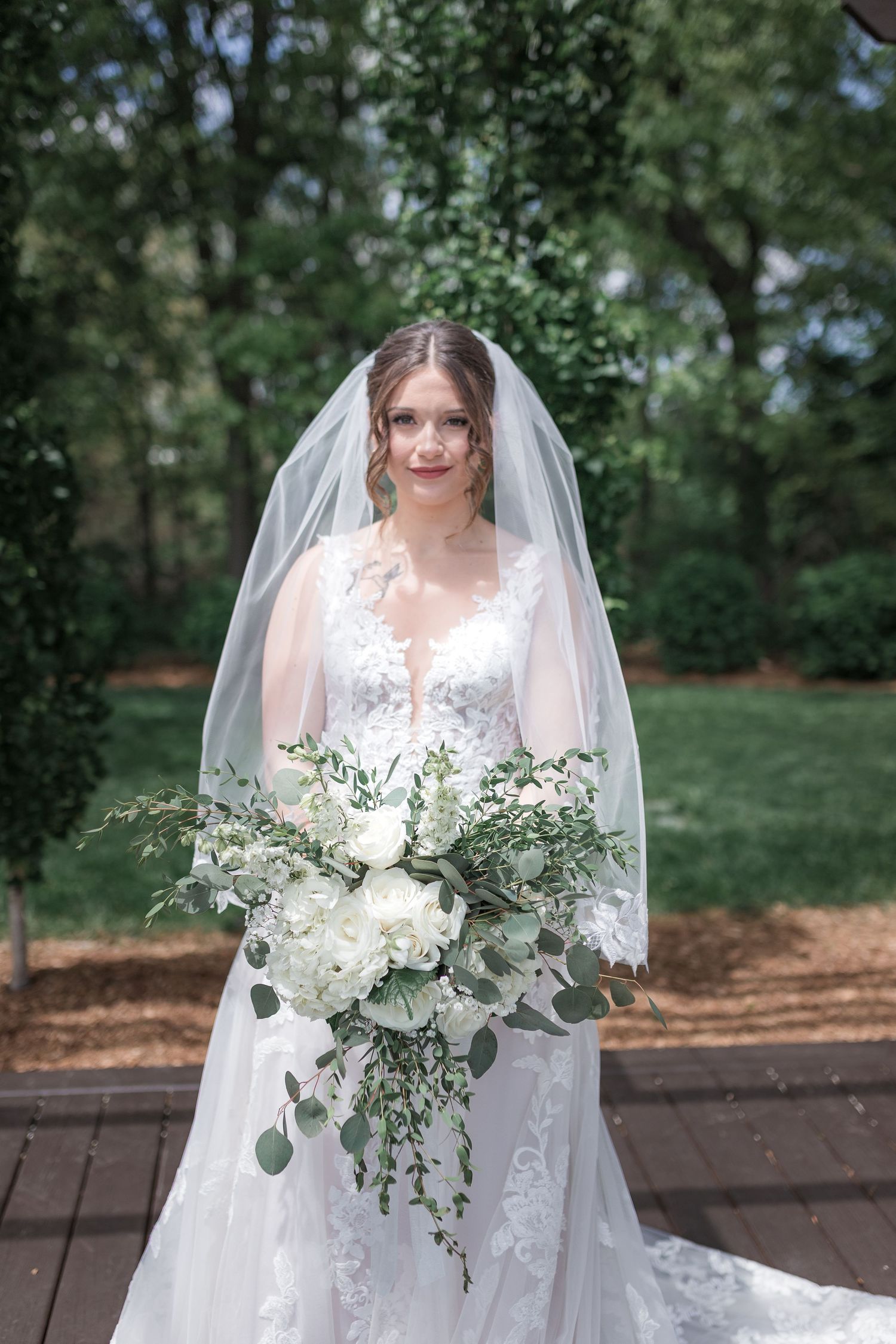 Elegant bride in white lace gown holds a cascading bouquet of white flowers and eucalyptus.
