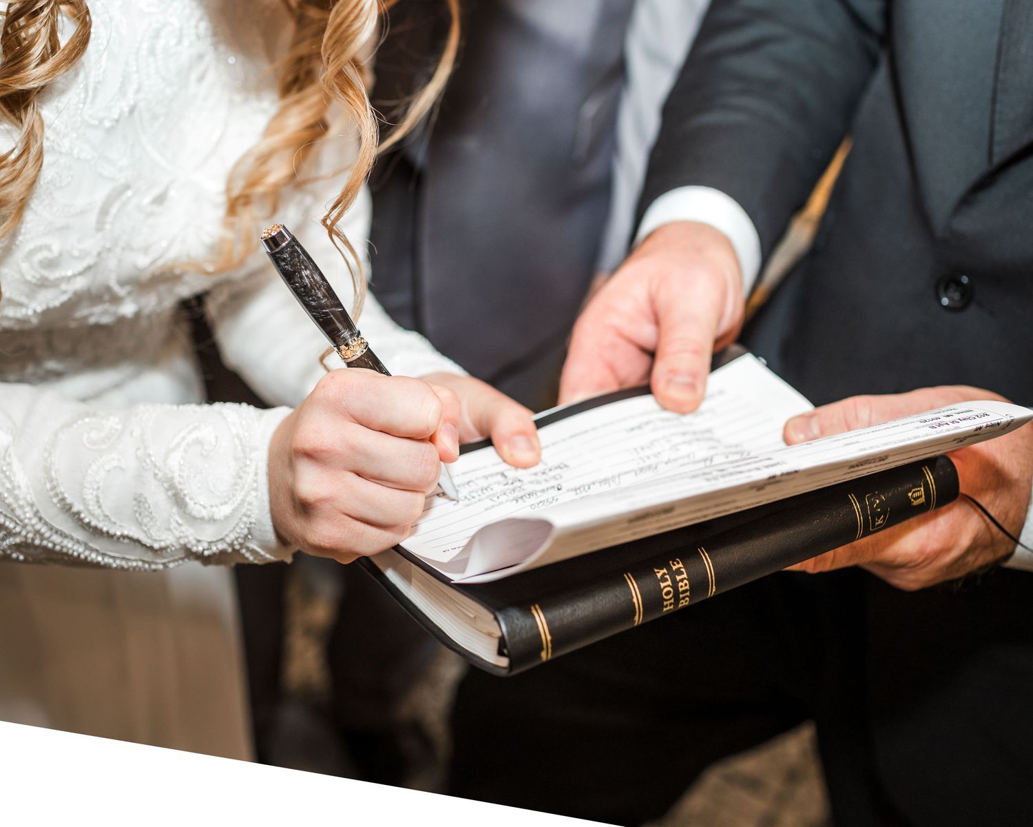 Close-up of hands signing a document with a pen during a wedding ceremony.