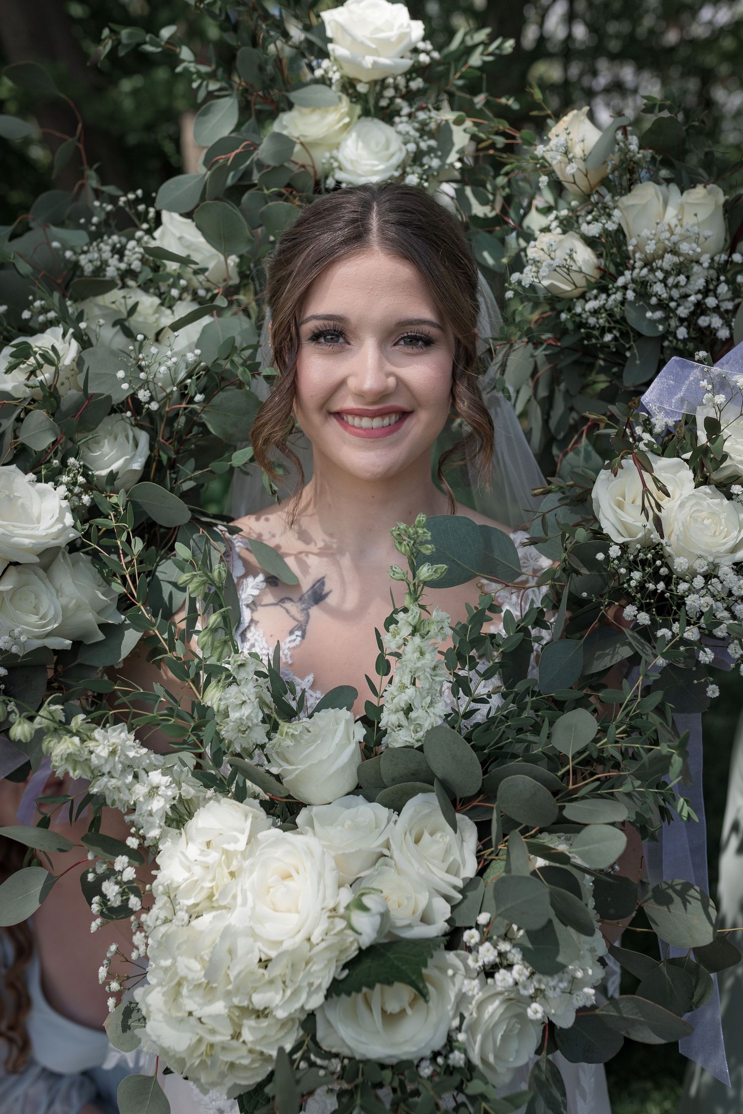 White roses and greenery frame a joyful bridal portrait in an outdoor garden setting.