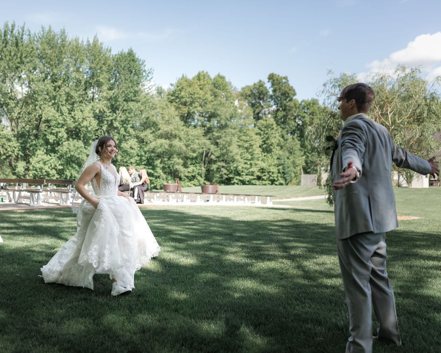 Couple walks hand in hand across sunny meadow during wedding photo session.