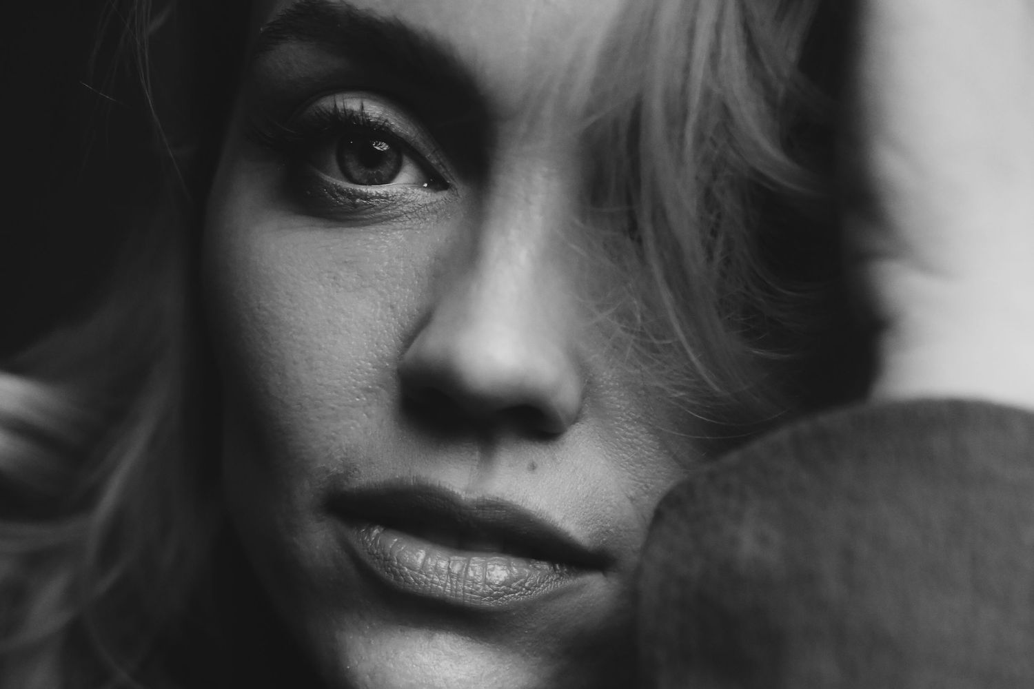 A dramatic black and white portrait photograph shows intense gaze and subtle smile against soft lighting.