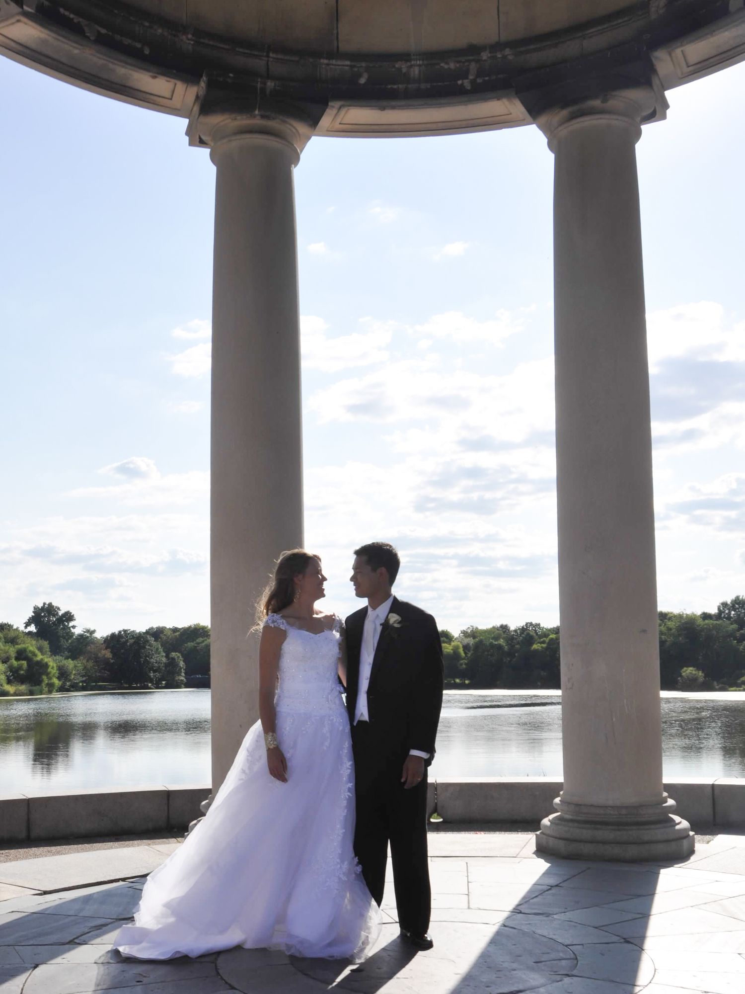 Bride and groom stand beneath the grand pillars of the FDR Park gazebo in Philadelphia, framed by elegant architecture.