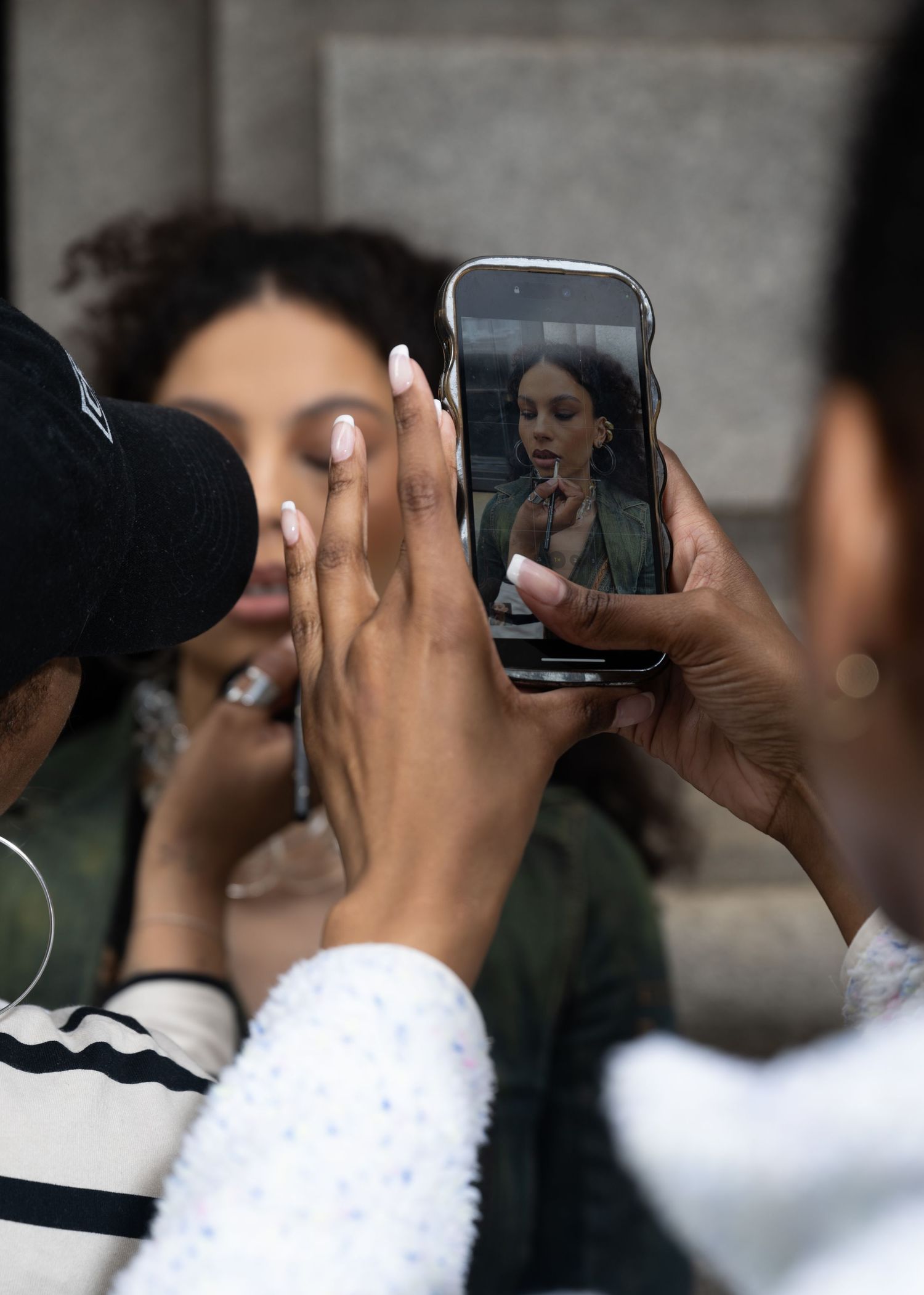 Hands holding smartphone to take photo of someone getting makeup applied.