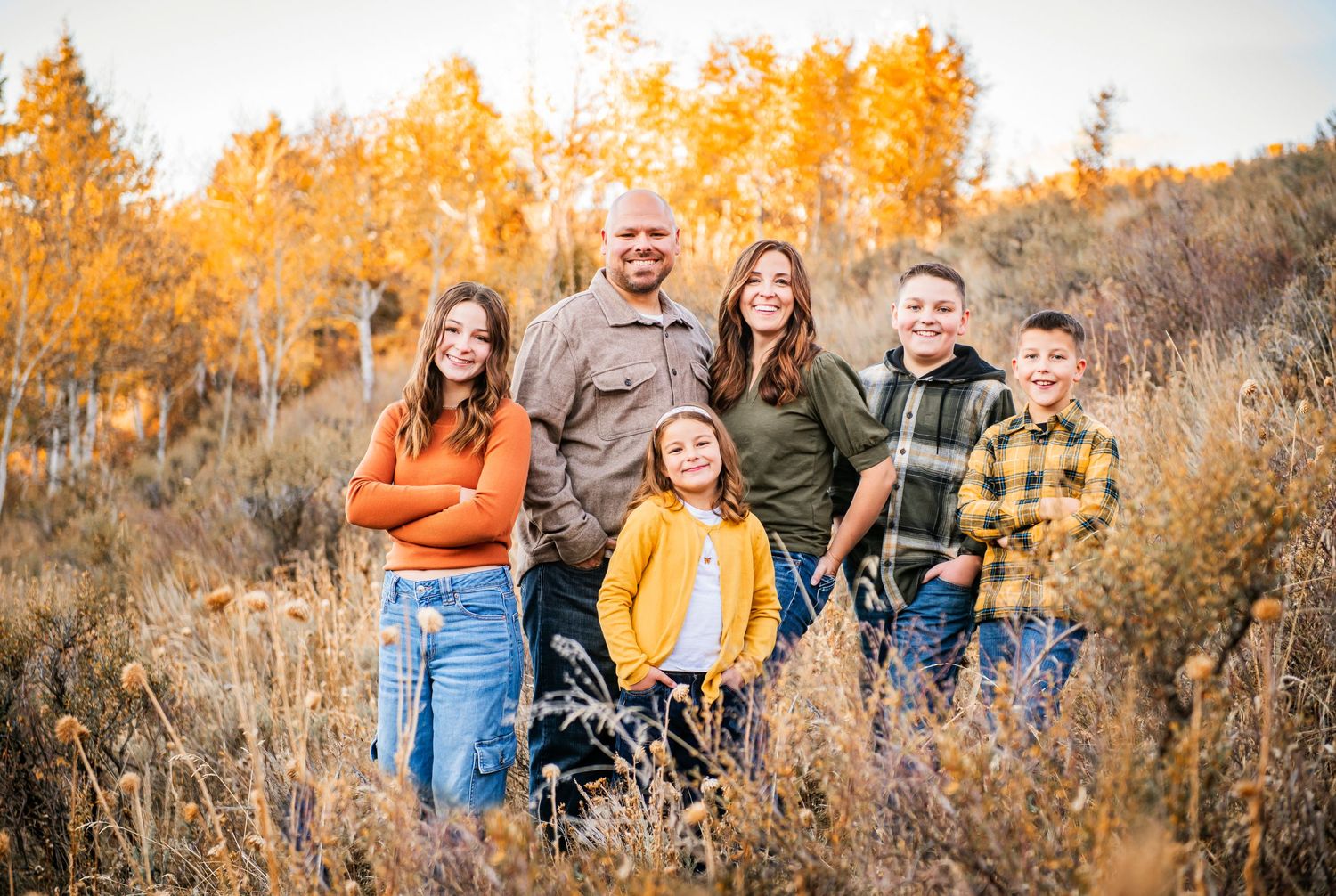 A group poses together in a golden autumn field filled with tall grass and aspen trees in fall colors.