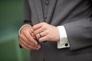 Close-up detail of groom's hands adjusting wedding ring on finger with cufflink visible.