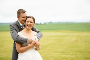 Newlyweds embrace and laugh together in an open green field.