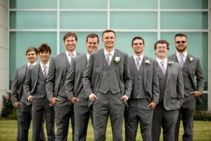Groomsmen in matching gray suits stand in a row against modern turquoise wall.