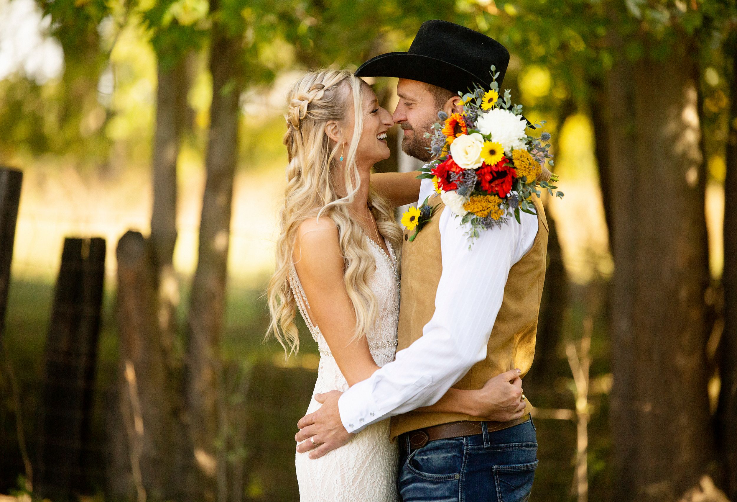 Romantic country wedding couple embracing at sunset with vibrant autumn flowers in a wooded setting.