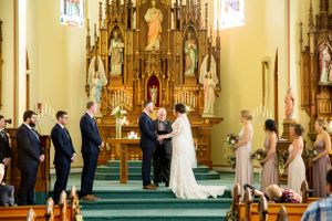 A traditional Catholic church wedding ceremony takes place at an ornate altar with stained glass windows and decorative woodwork.