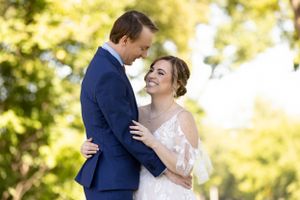 Elegant wedding couple sharing a joyful moment against sun-dappled trees.