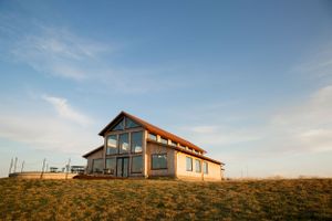 Modern house with large windows sits atop a grassy hill against blue sky at golden hour.
