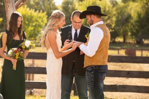 Outdoor wedding ceremony taking place in front of rustic wooden fence at sunset.