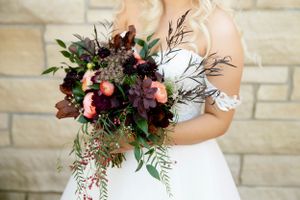 Elegant bridal bouquet with deep burgundy and pink flowers against stone wall.