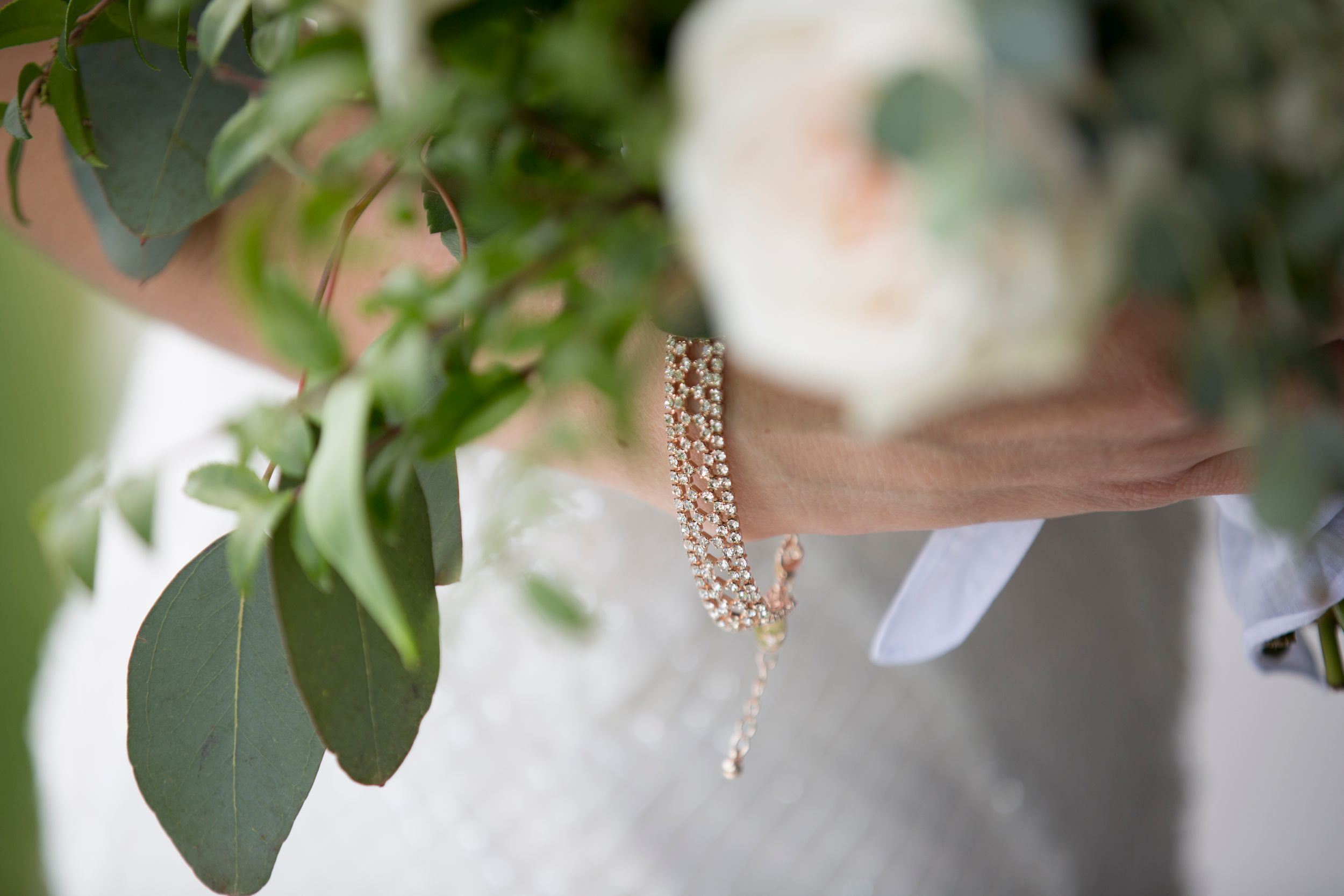 Delicate pearl earrings hang among green foliage in soft focus.