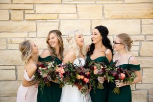 Bridal party in emerald green dresses hold lush burgundy bouquets.