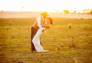 Romantic sunset wedding portrait with couple in rustic attire sharing an intimate moment.