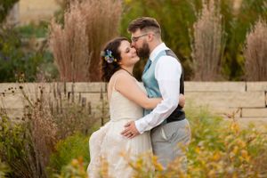 A romantic wedding photo of a couple embracing in a garden with soft autumn grass in the background.